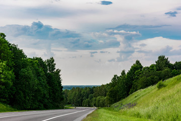 asphalt road with markings, a winding highway is located between trees and a hill with green grass