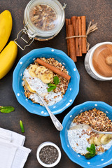 Morning breakfast for two. Yogurt with fruit, granola with cinnamon and chia seed in a plate on a concrete background.