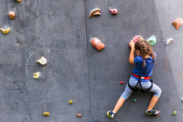 Beautiful young girl climbing to big artificial wall