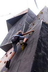 Beautiful young girl climbing to big artificial wall