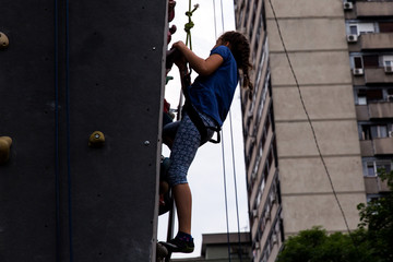 Fototapeta na wymiar Beautiful young girl climbing to big artificial wall