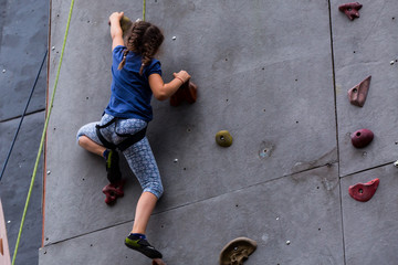 Beautiful young girl climbing to big artificial wall