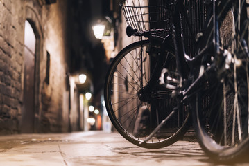 retro bicycle in the night old city on background bokeh light flare in night architecture, vintage bike in evening street in barcelona town, cycle transportation in defocus backdrop building