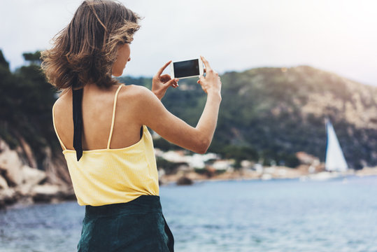 Hipster blogger girl holds mobile phone in female hands, take photo picture of natural seascape on a sunny summer day while travel and vacation, cellphone closeup on background ocean.