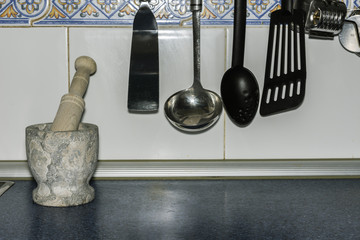 close-up hung kitchenware and a stone mortar with a tile background