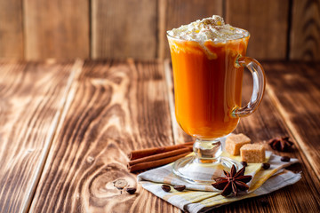 Pumpkin spice latte with whipped cream and cinnamon in glass on rustic wooden background