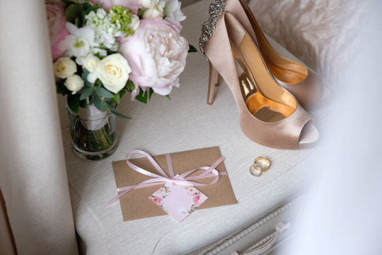 wedding gold rings, invitation card, bride's bouquet and shoes lie by the window
