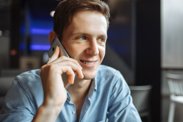 Happy young man, emotionally talking on the phone, sitting in a cafe, suitable for advertising, text insertion