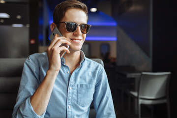 Happy young man in glasses, emotionally talking on the phone, sitting in a cafe, suitable for advertising, text insertion