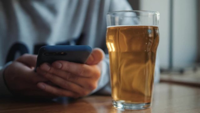 people, leisure and technology concept - close up of man with smartphone drinking beer and reading message at bar or pub