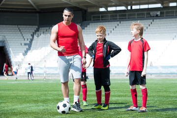 Full length portrait of junior football team practice, focus on coach explaining exercise, copy...