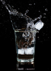 Splash of water with an ice cube in a glass on a black background