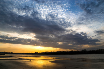 beautiful sunset on the river bank cloudy evening with reflection of sun rays on wet sand