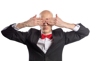 Slim bald elegant nerd in black suit with bow tie gesturing See No Evil. Isolated on white.