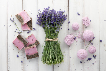 Lavender soap, bath bombs and beautiful lavender flowers on white wooden planks, top view. Natural skincare cosmetics.