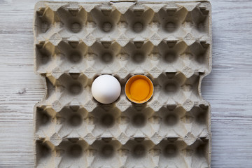 Whole and broken egg on tray, top view. White wooden background. From above.