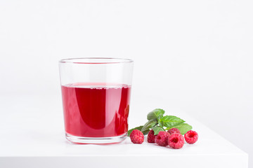 Fresh ripe raspberries and raspberry juice in a glass cup on a white background. Close-up, minimal concept of fashion food