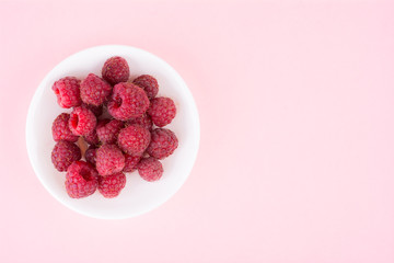 Fresh ripe raspberries on a white plate on a pink background. Close-up, top view, minimal concept of fashionable food, flatlay, copyspase