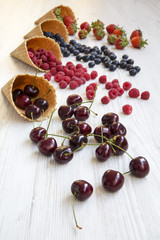 Waffle sweet ice cream cones with raspberries, cherries, strawberries and blueberries over white wooden background, side view.
