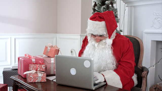 Modern Santa Claus working on his laptop and preparing presents