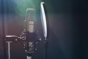 Close-up of modern microphone for song recording inside of dark studio in bright spotlight. 