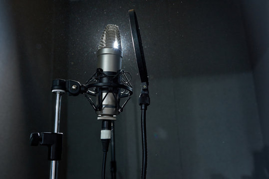 From below shot of professional recording microphone against bright spotlight in sound studio. 