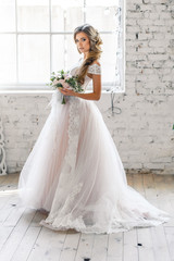Fototapeta premium A bride with hairstyle and make up in gorgeous pink wedding dress and a vail with a bouquet of peonies. A portrait of beautiful girl with brunette hair and blue eyes in studio