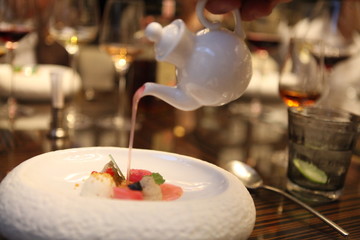 Tableside Service at customer's table by Professional Starred Chef. Pouring over to a luxury fine dining dessert in white stylish bowl. Final touch to perfect meal. Selective focus. Bokeh background. 