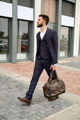 Attractive businessman walking down the street holding travel bag