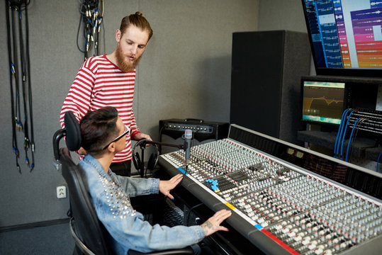 Man and woman sitting at control console in contemporary music recording studio and talking. 