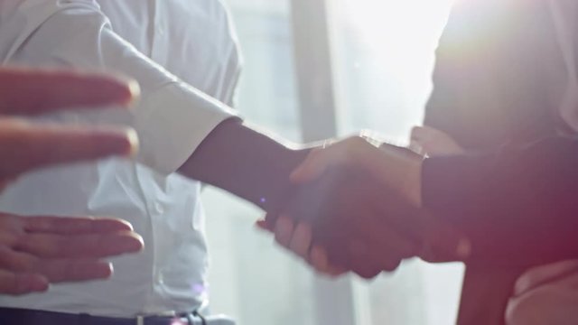 Tilt down shot of young African American businessman standing in the office with colleagues, talking and shaking hands with partner while making a deal