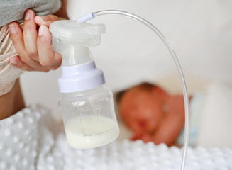 Automatic breast pump. Mothers breasts milk for newborn baby in bed room at home.
