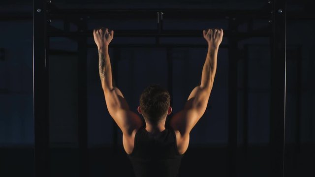 power muscular bodybuilder guy doing pullups in gym. Fitness man pumping up lats muscles.
