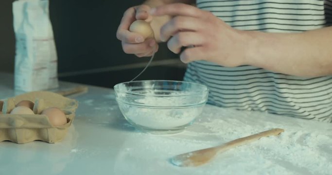 Young man cracking egg in kitchen