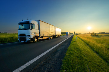 Fototapeta na wymiar Trucks driving on the asphalt road in a rural landscape in the golden sunset