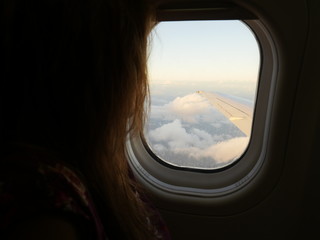 Passenger looking out the flying airplane window with view of clouds and wing