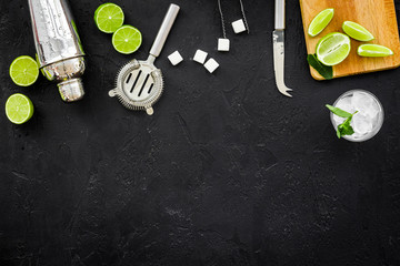 Make mojito cocktail with lime and mint. Shaker, strainer, glass near slices of lime on cutting board on black background top view copy space