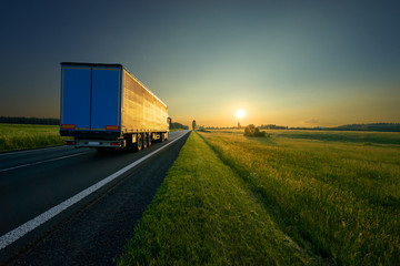 Truck driving on the asphalt road in a rural landscape in golden sunset colors