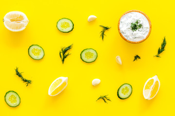 Greek yogurt dip with greenery, cucumber, oranges, garlic on yellow background top view pattern