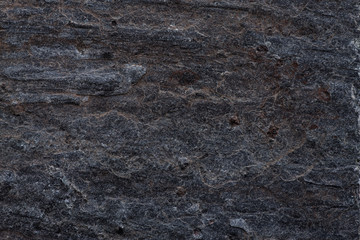 Close-up of a dark rock surface featuring natural striations and rugged texture, ideal for backgrounds, industrial designs, and architecture content.