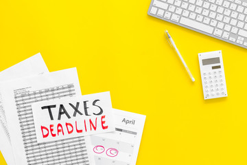 Taxes deadline words on office work desk with calendar and bills on yellow background top view copy space. Circled dates