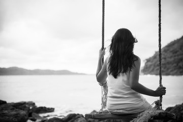 Black and white of Sad and lonely woman sitting alone on a the wooden swing over the sea