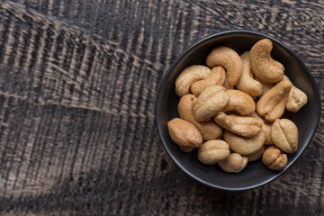 Raw cashew nuts in bowl on textured wooden background, table top view