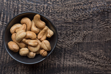Raw cashew nuts in bowl on textured wooden background, table top view