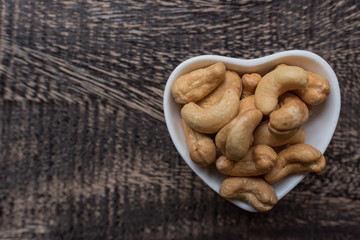 Raw cashew nuts in bowl on textured wooden background, table top view