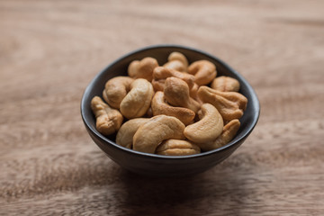 Raw cashew nuts in bowl on textured wooden background, table top view