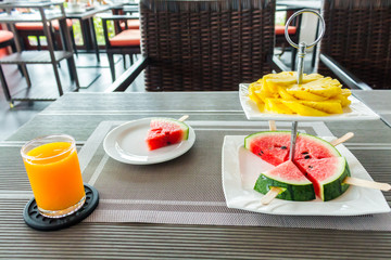 Flatlay slide fruit decoration in tier on table./ Flatlay slide fruit, pineapple, watermelon decoration in tier with orange juice on table for breakfast.