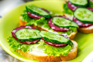 sandwiches with sausage smoked and  green cucumber and lettuce leaves