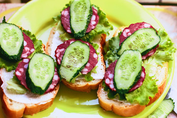 sandwiches with sausage smoked and  green cucumber and lettuce leaves