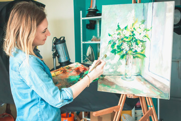 girl artist with a palette of paints draws paintings in an art studio. Palettes and easel,